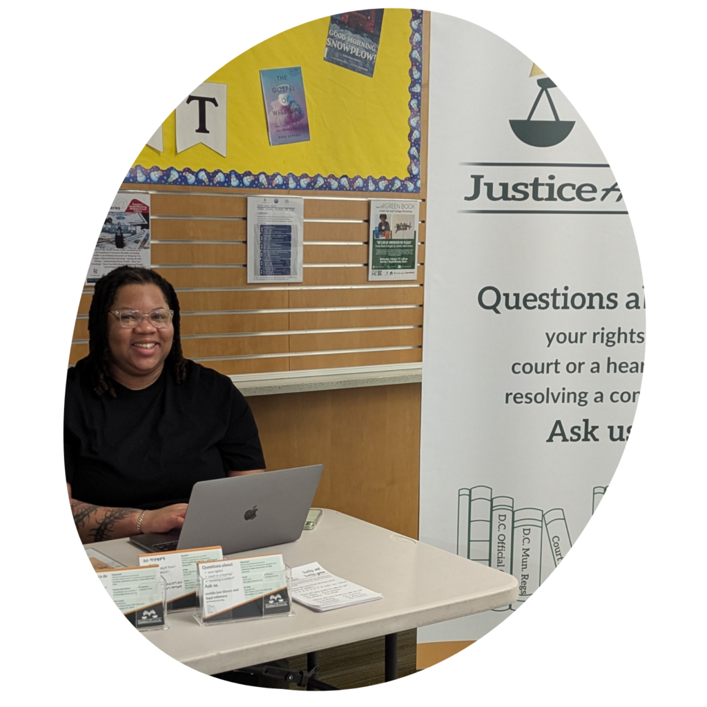 young Black woman at the reference desk with an open laptop in front of her and JusticeAccess postcards on the table